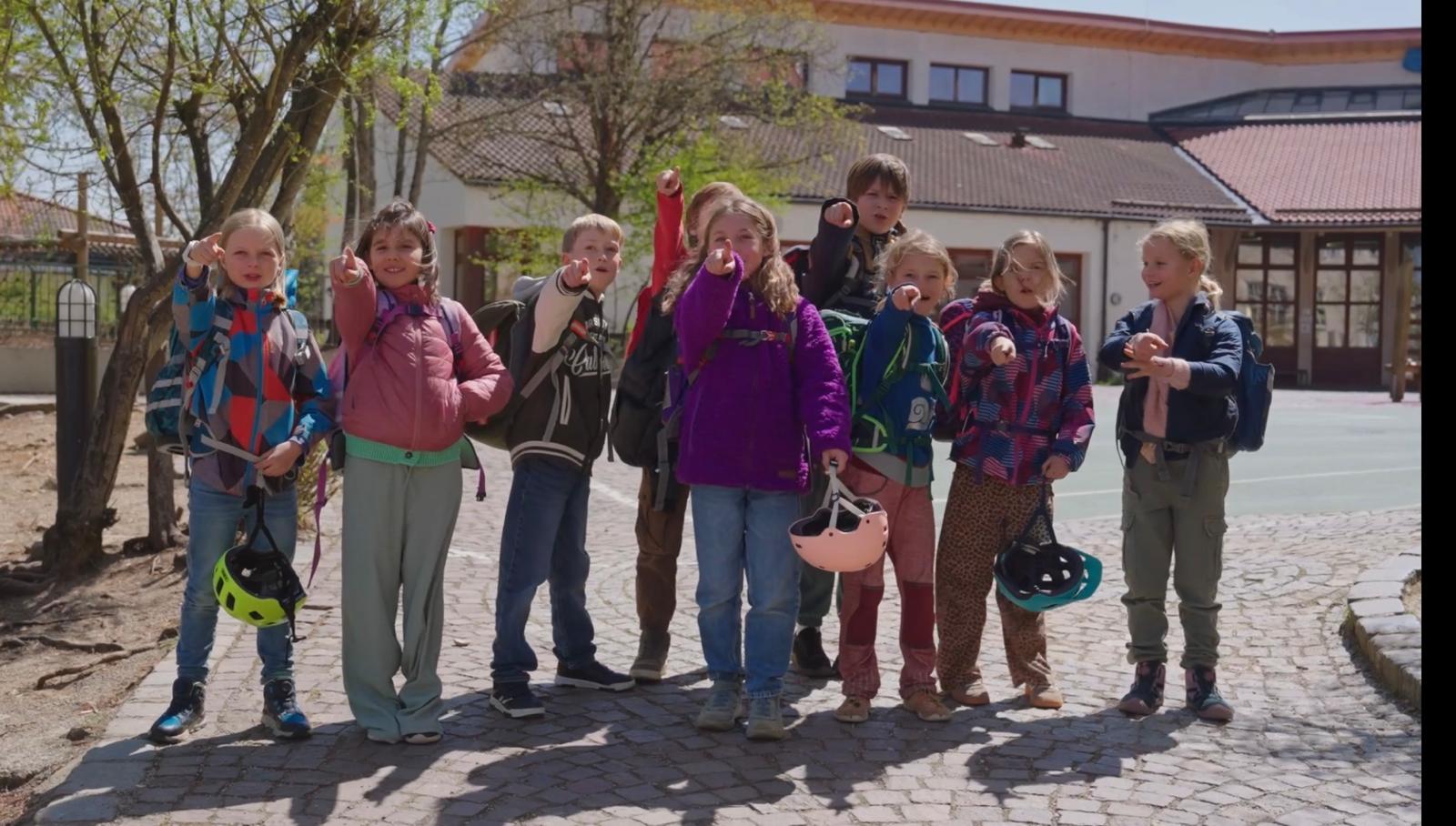 Eine Gruppe von Grundschulklassen-Kindern läuft selbstständig, gut gelaunt und sicher mit ihren Schulranzen über einen Gehweg zur Schule.